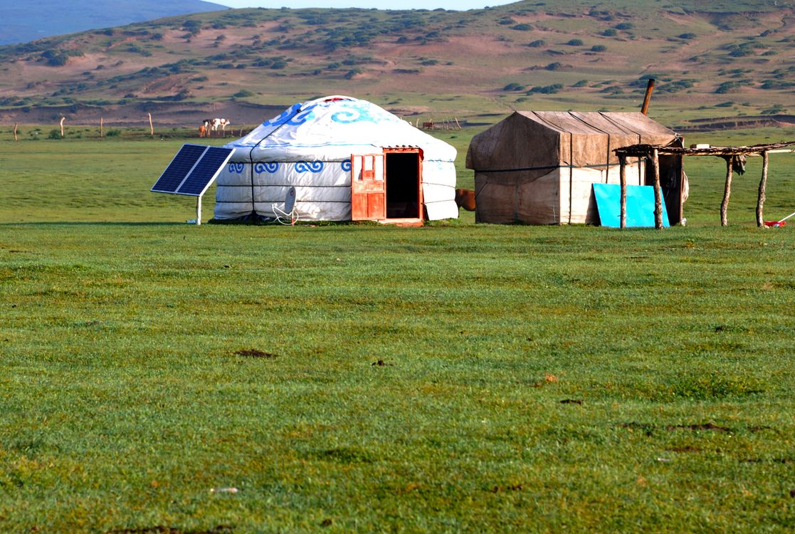 Off-grid solar panel beside a traditional ger in an open grassy landscape