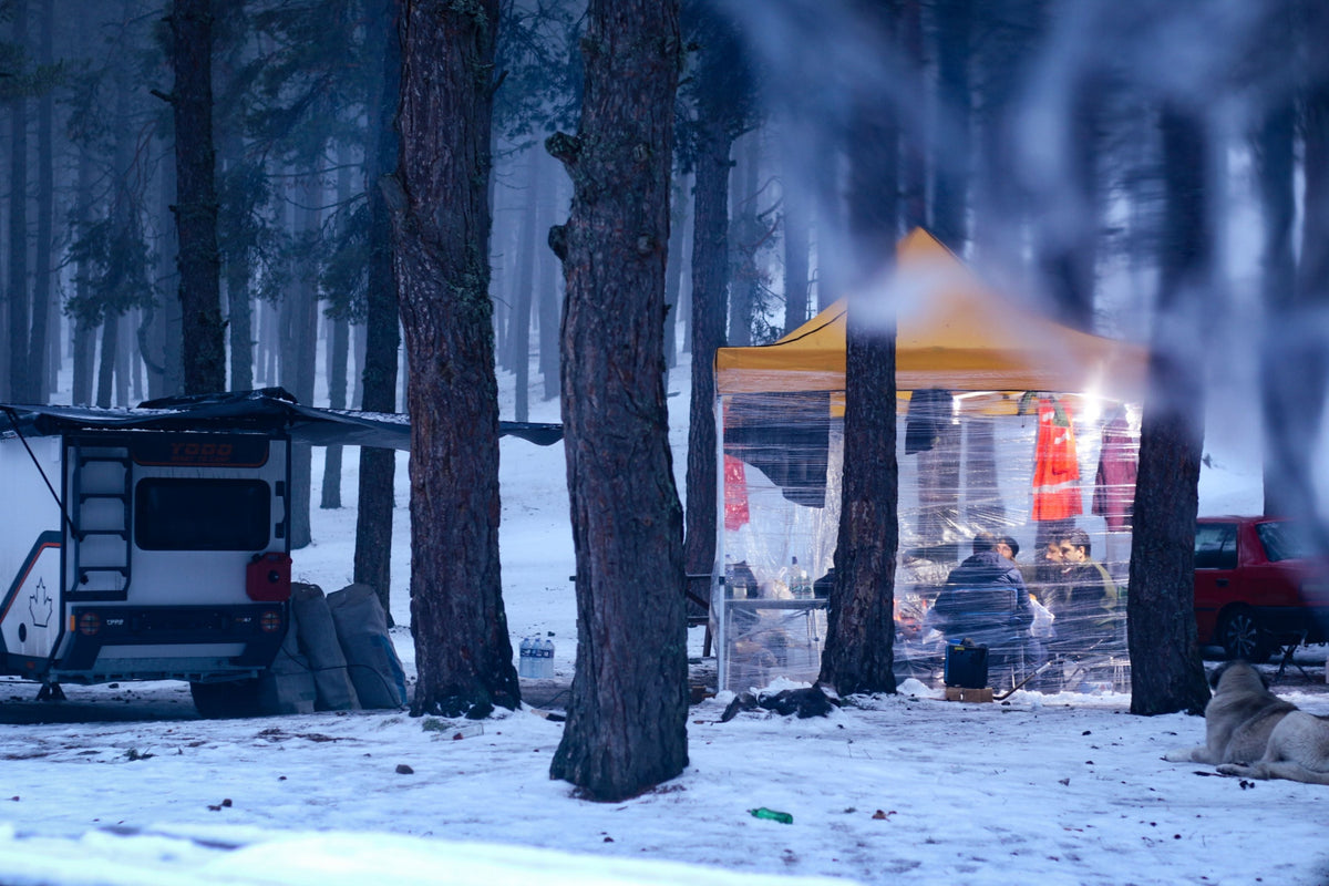 Winter campsite with a camper and tent in a snowy forest